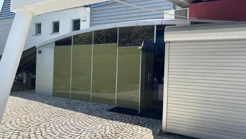 Moderne Gebäudefassade mit geschwungenen Glasfronten, einem Rolltor und gepflastertem Vorplatz.