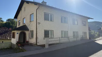 Traditionelles Mehrfamilienhaus mit heller Fassade und Satteldach in ländlicher Umgebung.