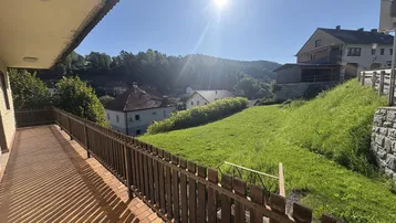 Langer Balkon mit Holzgeländer und weitem Blick auf die grüne Hügellandschaft.