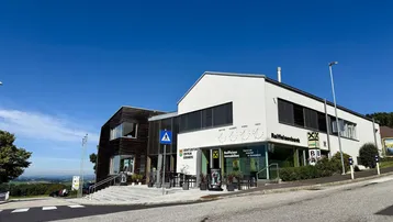 Modernes Geschäftsgebäude mit weißer und holzverkleideter Fassade an einer Straße mit Weitblick.