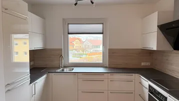 Moderne Küche mit weißen Hochglanzfronten, dunkler Arbeitsplatte und Blick ins Grüne.