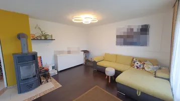 Helles Wohnzimmer mit gemütlichem Ecksofa, Holzofen und moderner Deckenleuchte.