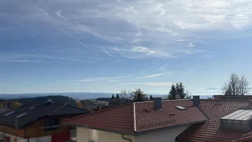 Weitblick über Dächer und eine malerische Landschaft mit fernen Bergen unter blauem Himmel.