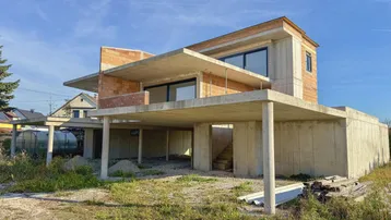 Moderner Neubau im Rohbauzustand mit großen Fensterfronten und massiver Betonkonstruktion.