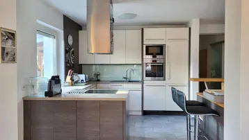 Moderne Küche mit Kochinsel, integrierten Geräten und stilvoller Dunstabzugshaube.