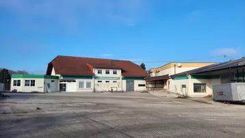 Außenansicht eines Lagerhausmarktes mit großem asphaltierten Parkplatz unter blauem Himmel.
