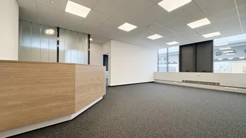 Geräumiger Büroraum mit Teppichboden, großen Fenstern und einer modernen Rezeptionstheke.