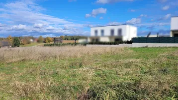 Weitläufiges Grundstück mit Blick auf die grüne Landschaft und moderne Gebäude im Hintergrund unter blauem Himmel.