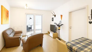 Helles Wohnzimmer mit bequemen Ledersofas, Holzboden und Zugang zu einer Terrasse.