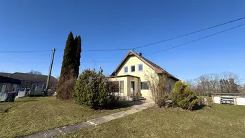Gelbes Einfamilienhaus mit Satteldach und Vorgarten an einem sonnigen Tag.