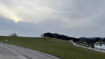 Weitläufige grüne Hügellandschaft unter bewölktem Himmel mit einem Sonnenstrahl am Horizont.