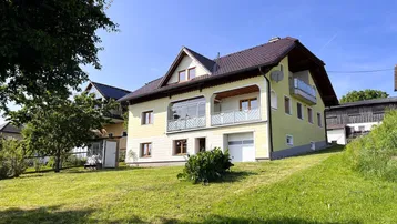 Rückansicht des Hauses mit großem Garten und Balkonen unter strahlendem Sonnenschein.