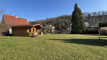 Großer Garten mit Rasenfläche und einem charmanten Holzgartenhaus unter blauem Himmel.