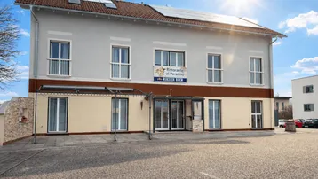 Mehrstöckiges Gebäude mit heller Fassade, Solarpaneelen auf dem Dach und einem Restaurant im Erdgeschoss.