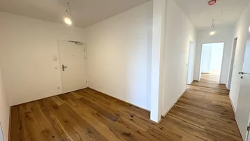 Heller Eingangsbereich mit robustem Holzfußboden und Zugang zu weiteren Räumen in einem Neubau.