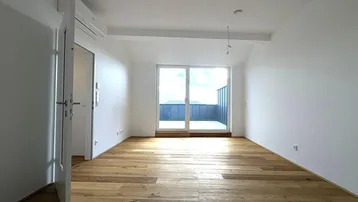 Helles Zimmer mit Holzboden und Zugang zu einem Balkon, ideal als Wohn- oder Schlafbereich.
