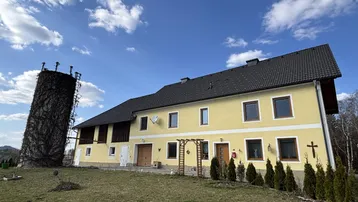 Gelbes Landhaus mit dunklem Dach und einem von Efeu bewachsenen Turm unter blauem Himmel.