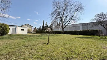 Großer Gartenbereich mit Rasenfläche, Bäumen und einem Nebengebäude unter blauem Himmel.