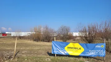 Blick auf ein unbebautes Grundstück mit einem 'Immobilie zu kaufen'-Banner unter klarem blauem Himmel.