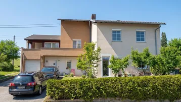 Ansicht des Einfamilienhauses mit Vorgarten, Hecke und Stellplätzen für Fahrzeuge.