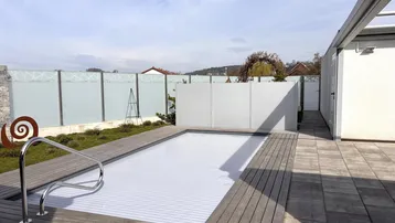 Moderner Außenbereich mit überdachtem Pool, Holzdeck und Sichtschutzwand.