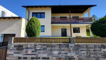Vorderansicht des Hauses mit Balkon, Steinmauer und gepflegtem Vorgarten.