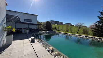 Sonnige Terrasse mit großem Pool, Außenküche und weitem Blick auf die grüne Landschaft.