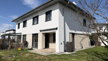 Modernes Einfamilienhaus mit weißer Fassade, großen Fenstern und gepflegtem Gartenbereich.