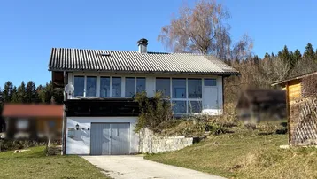 Hausfassade mit integrierter Garage, großen Fenstern und einem Gartenbereich in ländlicher Umgebung.