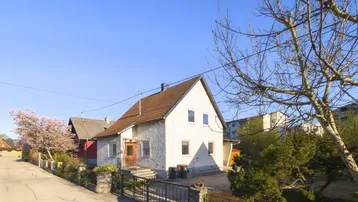 Vorderansicht des Einfamilienhauses von der Straße aus mit Vorgarten und blühendem Baum.