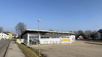 Gebäudeansicht eines modernen Gewerbeobjekts mit großem Parkplatz und barrierefreiem Zugang.