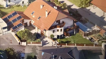 Luftaufnahme des Anwesens mit Photovoltaikanlage auf dem Dach und umliegender Bebauung.