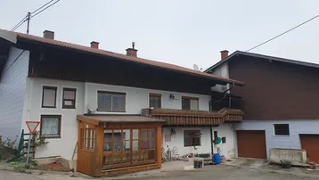 Traditionelles Haus mit weißer Fassade, Holzbalkon und einem verglasten Wintergartenanbau.