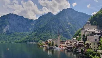 Malerische Ansicht eines Dorfes am See, umgeben von majestätischen Bergen unter blauem Himmel.