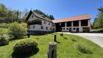 Großzügiges Anwesen mit traditionellem Gebäude, umgeben von grüner Natur und Bäumen unter blauem Himmel.