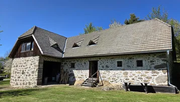 Altes Bauernhaus mit charakteristischer Steinfassade und Ziegeldach in ländlicher Umgebung.