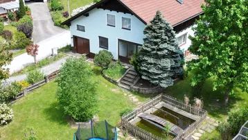 Luftaufnahme eines Einfamilienhauses mit großem Garten, Trampolin und Teichanlage.
