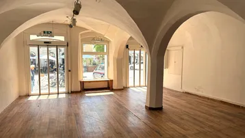 Geräumiger Gewerberaum mit Holzboden, Gewölbedecken und großen Fenstern zur Straße hin, ideal für Laden oder Galerie.
