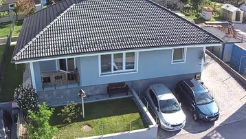Luftaufnahme eines gepflegten Einfamilienhauses mit Satteldach, Garten und Stellplätzen für Fahrzeuge.