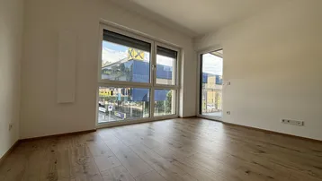 Helles Zimmer mit Holzboden und großem Fenster, das Zugang zu einem Balkon bietet.