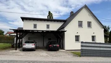 Modernes Einfamilienhaus mit weißer Fassade, Satteldach und einem Carport für zwei Fahrzeuge.