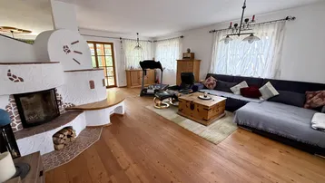 Gemütliches Wohnzimmer mit Holzboden, großem Sofa und traditionellem Kaminofen als Blickfang.