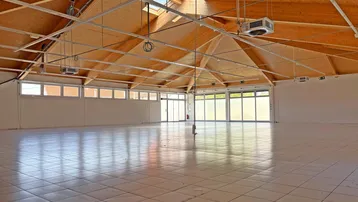 Großer, heller Innenraum mit hohen Holzdecken, Fliesenboden und großen Fenstern, ideal für gewerbliche Nutzung.