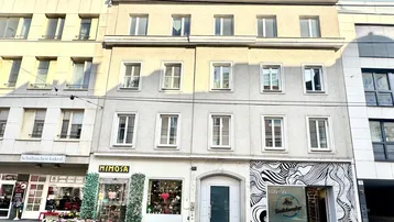 Mehrstöckiges Gebäude mit Geschäften im Erdgeschoss und Wohnungen darüber in einer städtischen Umgebung.