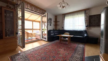 Gemütliches Wohnzimmer mit traditionellem Teppich, Ledersofa und Zugang zum Wintergarten.