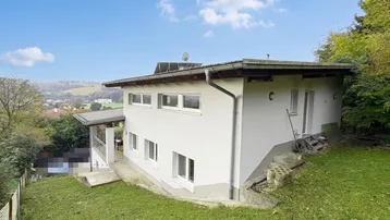 Weißes Einfamilienhaus mit Satteldach, umgeben von einem grünen Garten und weitem Blick über die Landschaft.