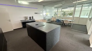 Modernes Büro mit Kücheninsel, Sitzbereich und Besprechungsraum hinter Glaswänden für kreatives Arbeiten.
