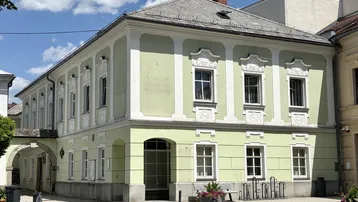 Historisches Gebäude mit hellgrüner Fassade und dekorativen Fensterrahmen an einem sonnigen Tag.