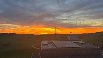 Spektakulärer Sonnenuntergang über ländlicher Landschaft mit Solaranlage auf dem Dach.