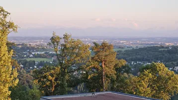 Weitläufiger Panoramablick über die Stadt und die umliegende grüne Landschaft mit Bergen im Hintergrund.
